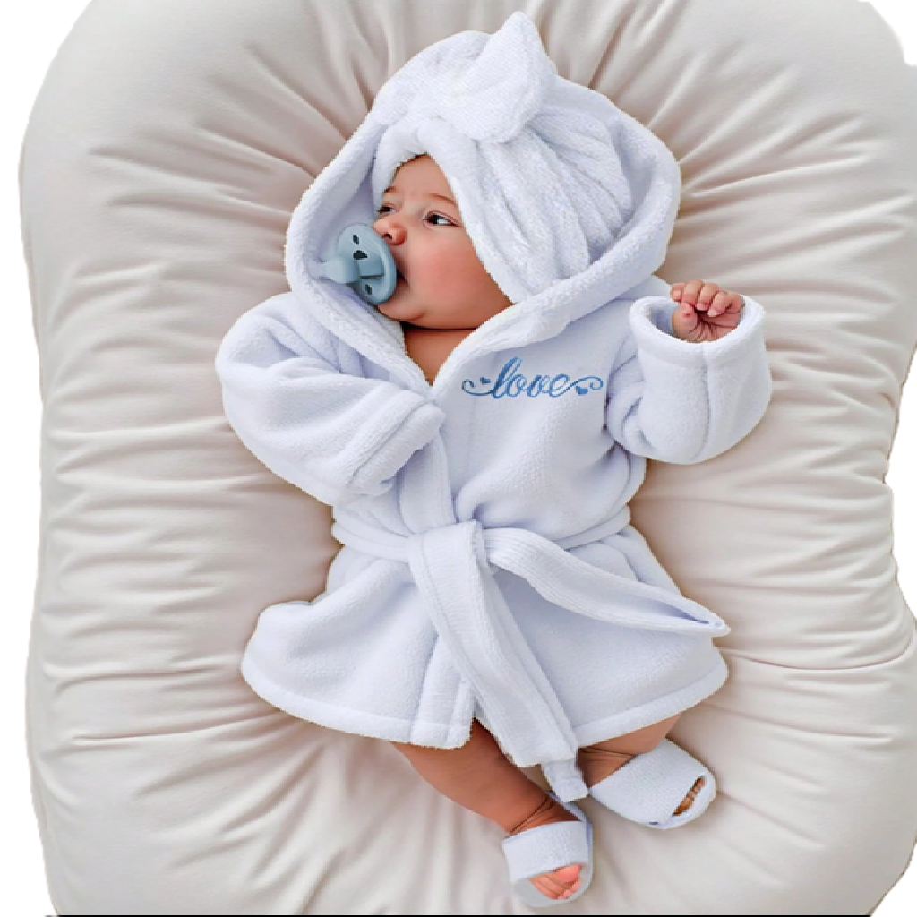Baby in a white robe with 'love' embroidered on it, lying on a white cushion.