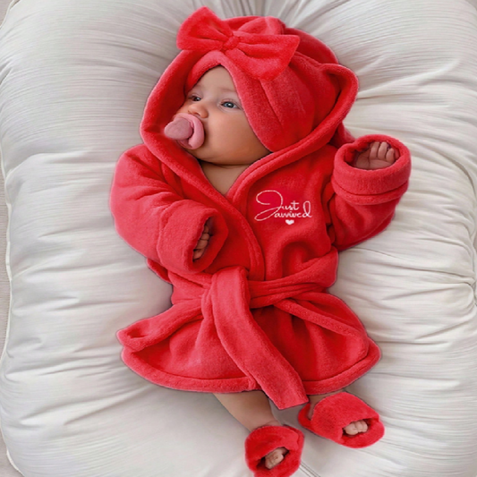 Baby in a red hooded outfit with a bow on a white background