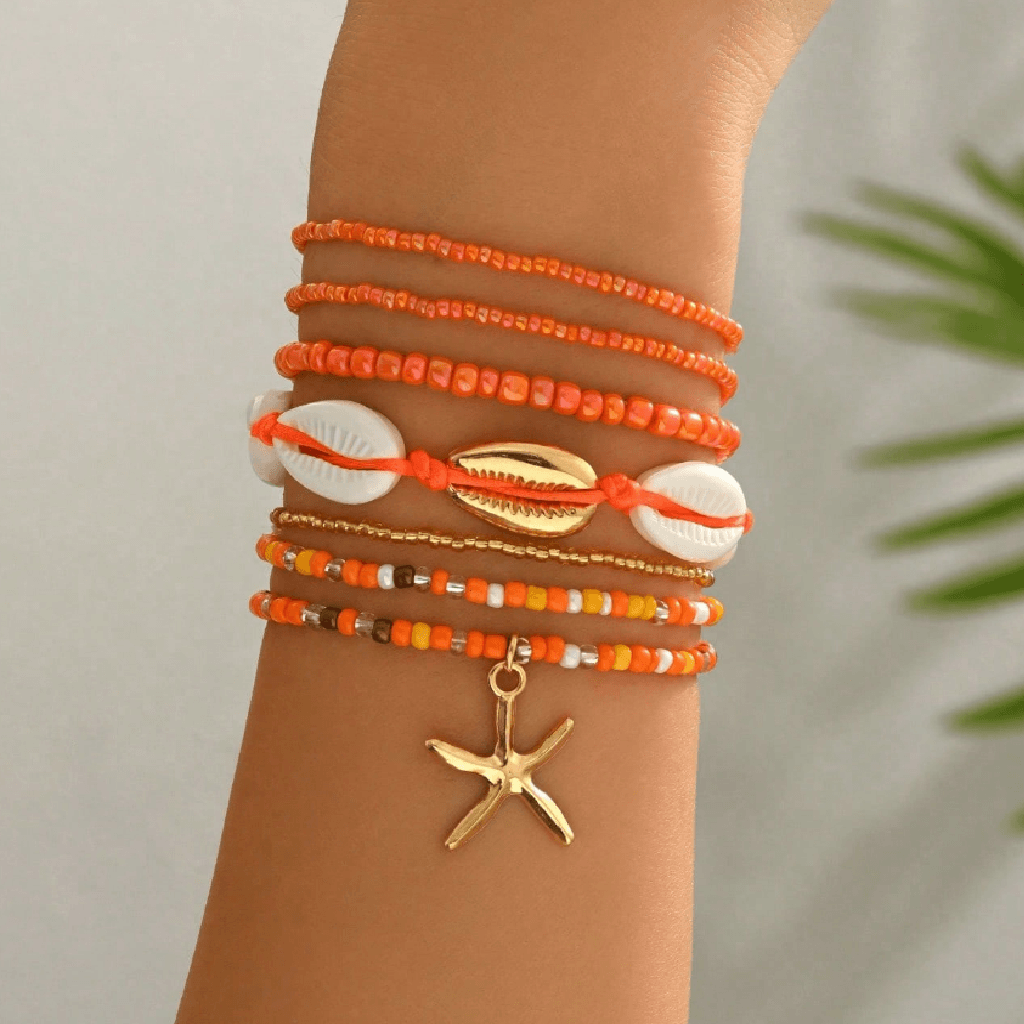 A stack of orange and white beaded bracelets with a gold starfish charm, worn on a person's wrist.