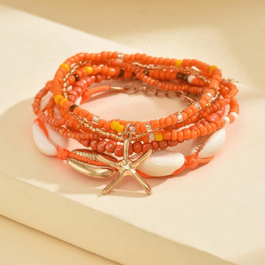 A stack of multi-strand beaded bracelets with orange and white cowrie shells and a gold-toned starfish charm, displayed on a beige surface.