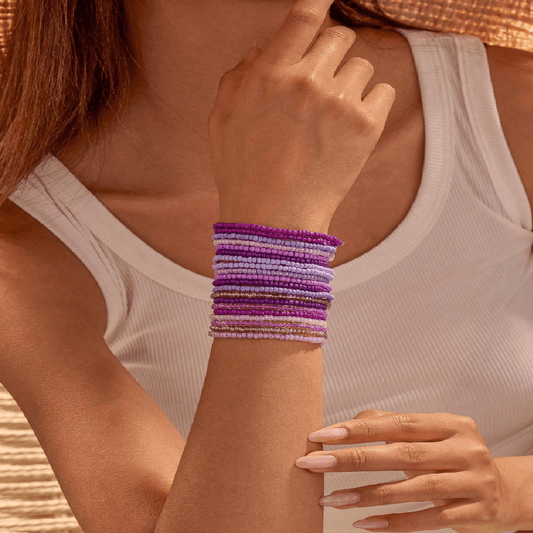 Woman wearing a stack of colorful beaded bracelets on a neutral background