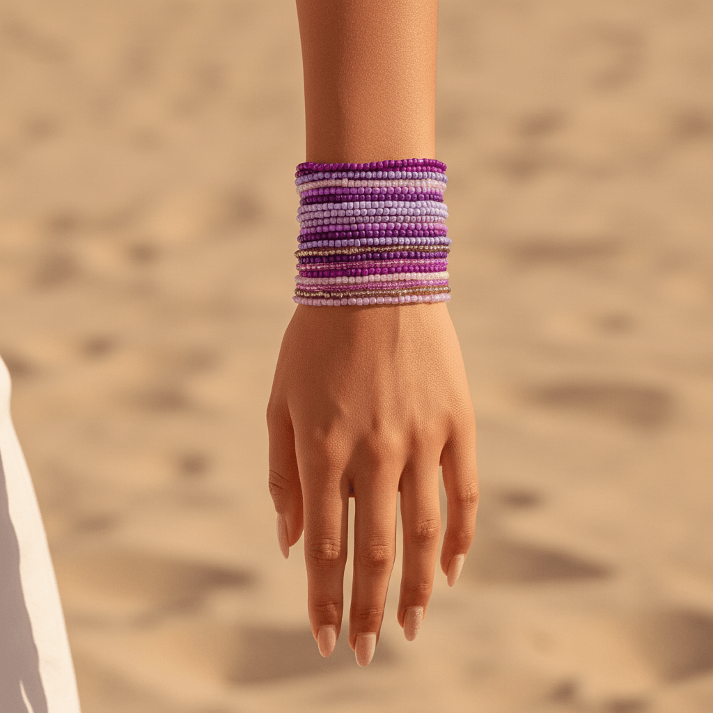 Hand wearing a purple bracelet against a sandy background