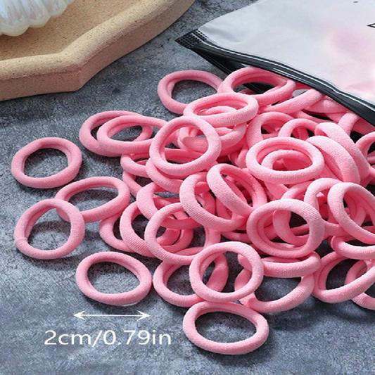 Pile of pink hair ties on a gray surface with measurement text.