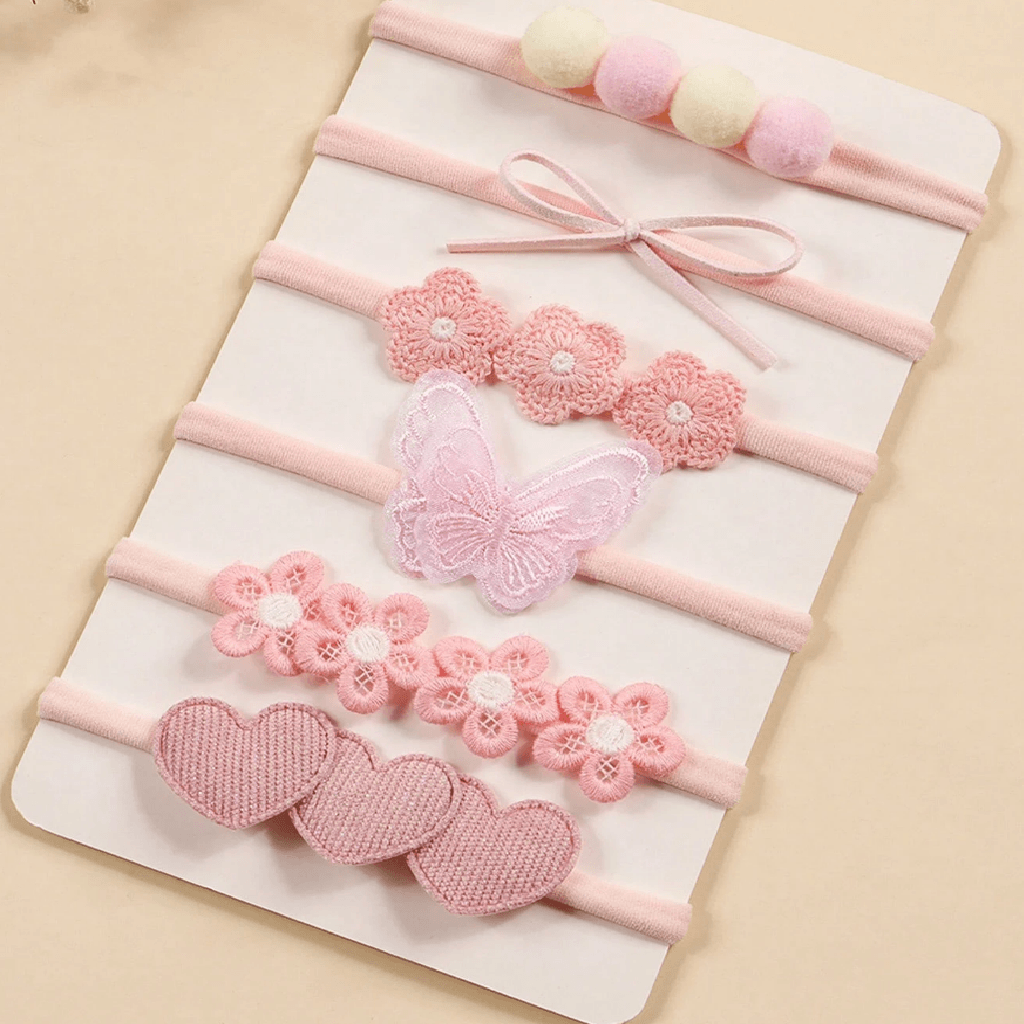 Set of pink baby headbands with floral and heart designs on a beige background