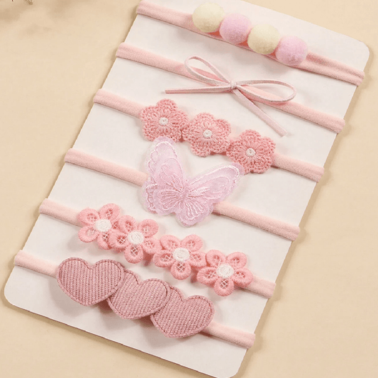 Set of pink baby headbands with floral and heart designs on a beige background