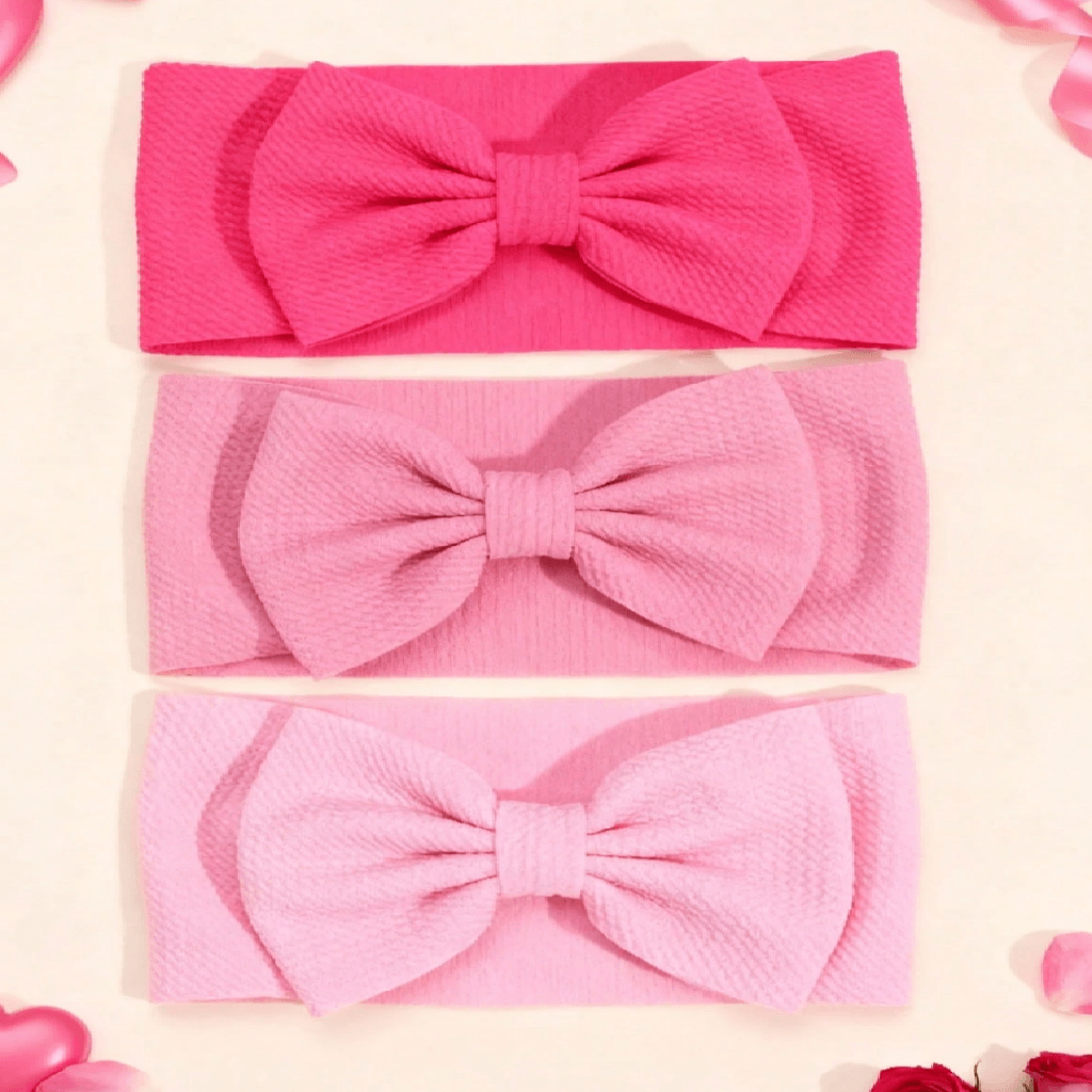 Three textured fabric headbands with large bows, shown in hot pink, light pink, and pale pink, arranged vertically on a light cream background with decorative rose petals.