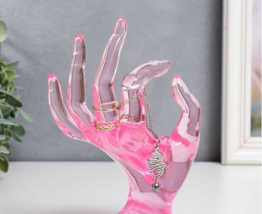 Pink acrylic hand-shaped jewelry holder with rings and a necklace 
