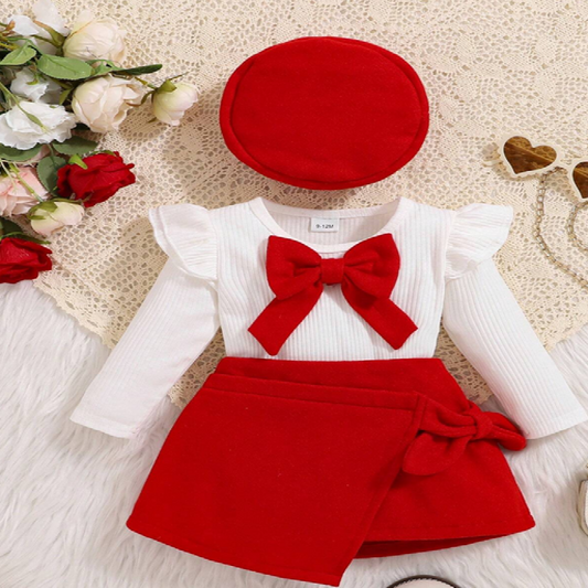 Children's outfit with red shorts, white shirt, and red hat on a textured surface with flowers.