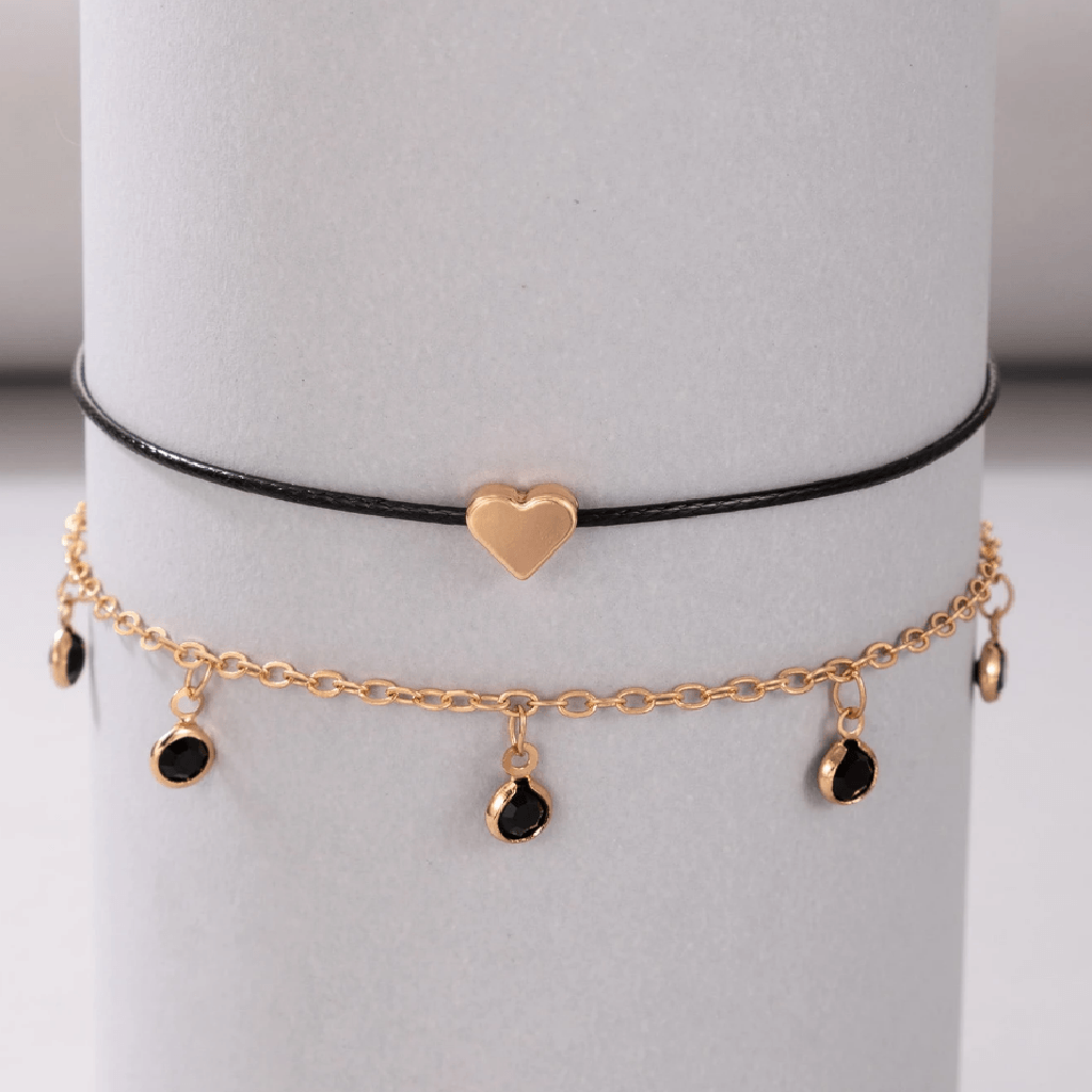 Gold anklet with heart charm and black beads on a white stand