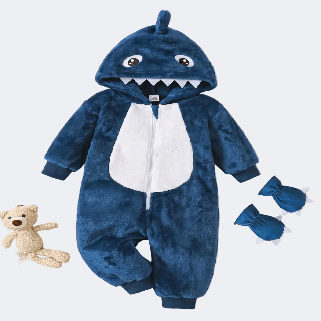 Blue shark-themed baby onesie with a white shirt, hood, and tail, accompanied by a teddy bear and booties on a light gray background.
