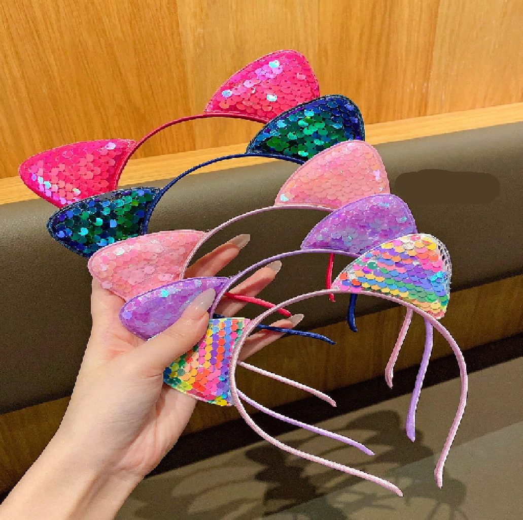 Colorful sequin cat ears held by a hand against a wooden background