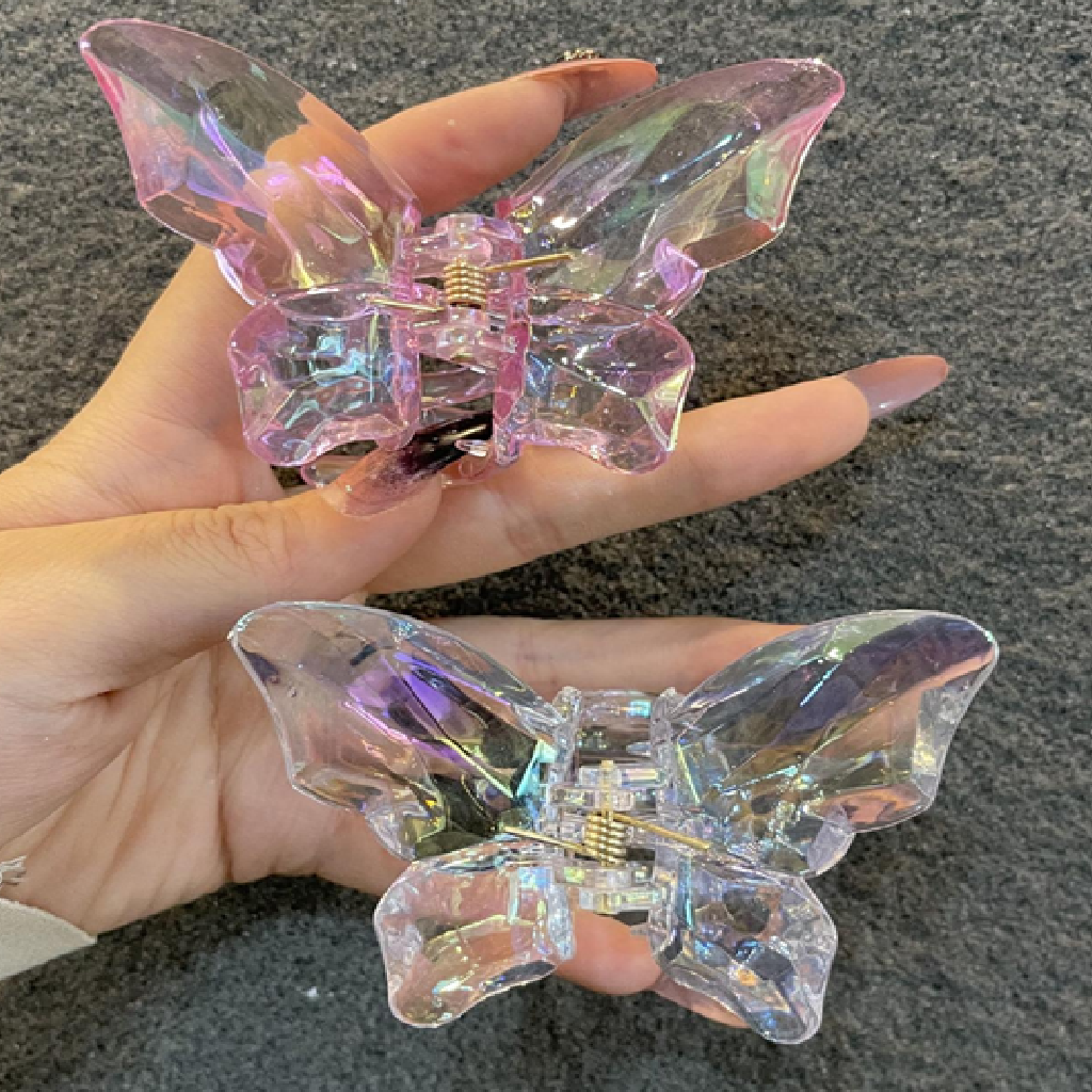 Clear butterfly-shaped hair clips held in a hand against a dark background