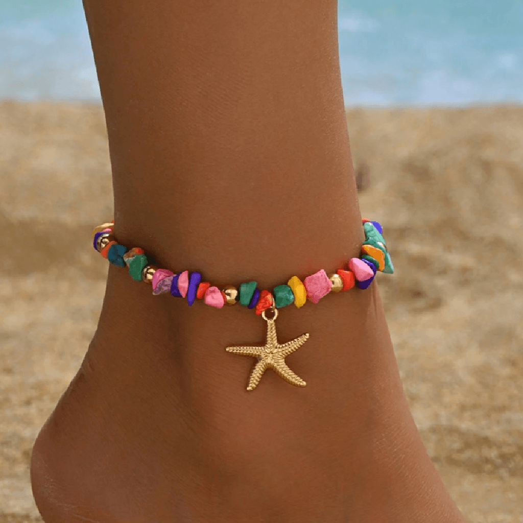 Colorful beaded anklet with a starfish charm on a person's ankle against a beach background.