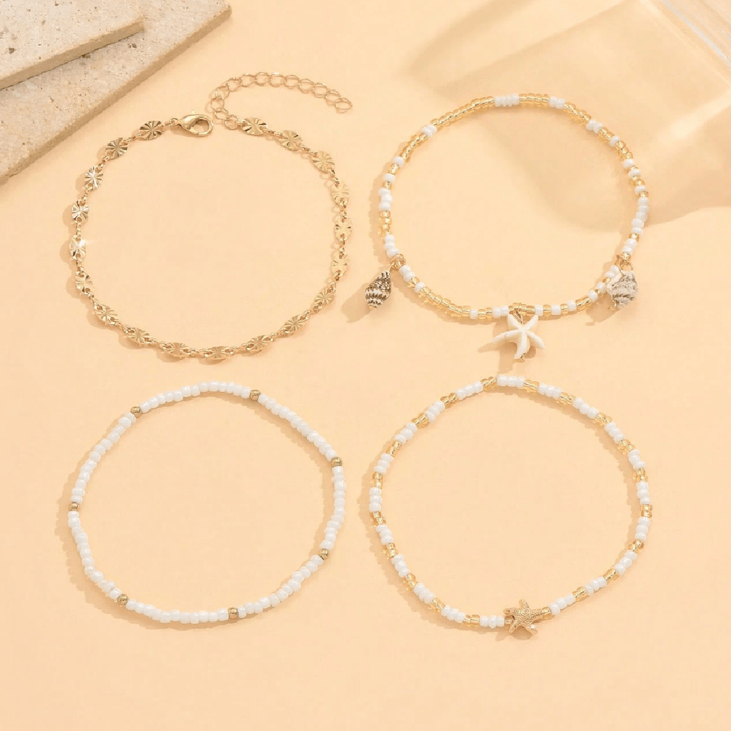 Set of four gold and white beaded bracelets on a beige surface