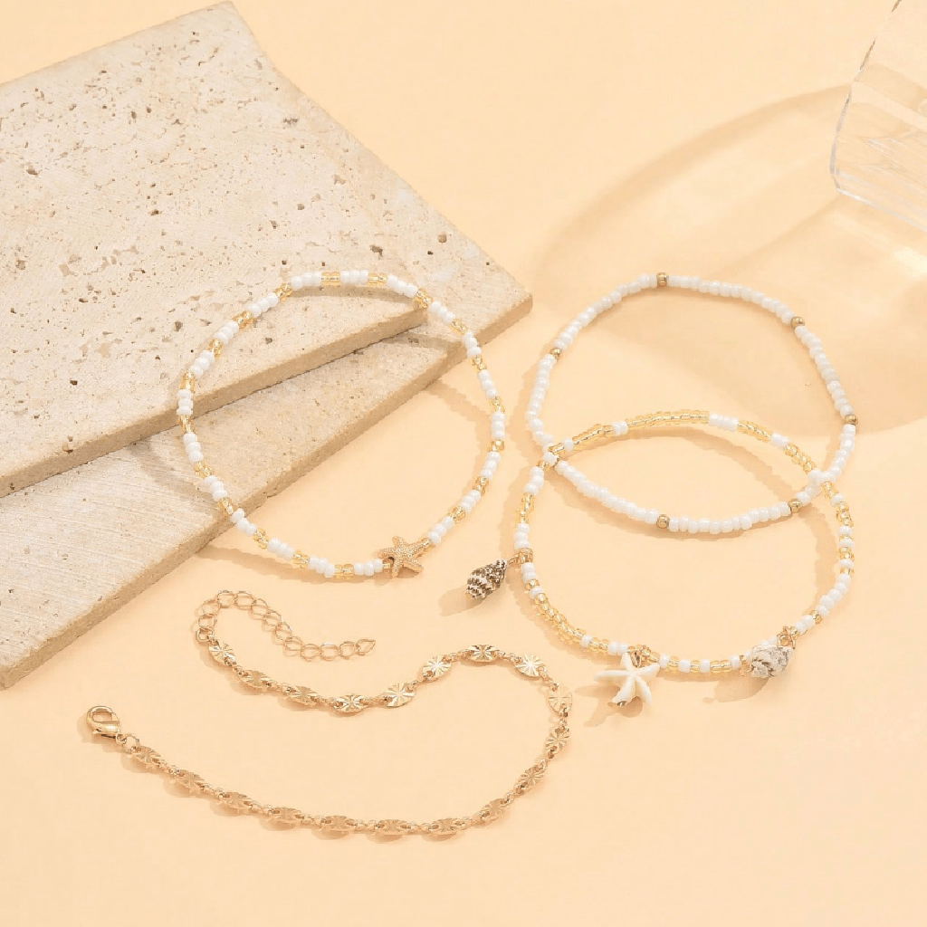 Set of four gold and white beaded bracelets on a beige surface