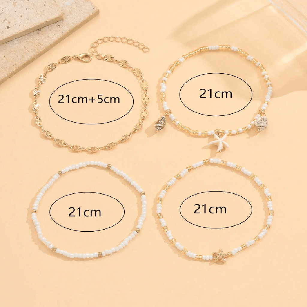Set of four gold and white beaded bracelets on a beige surface
