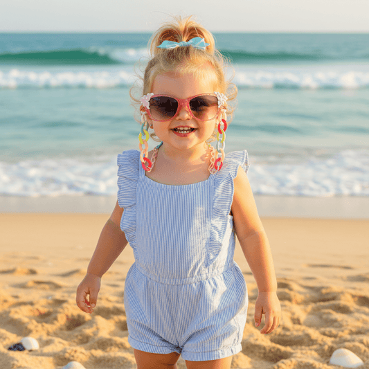 Child wearing sunglasses and a blue romper on a beach