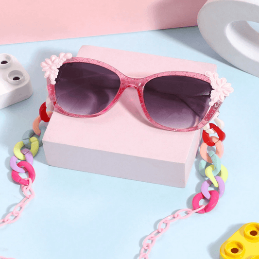 Pink sunglasses with floral and chain details on a light blue background