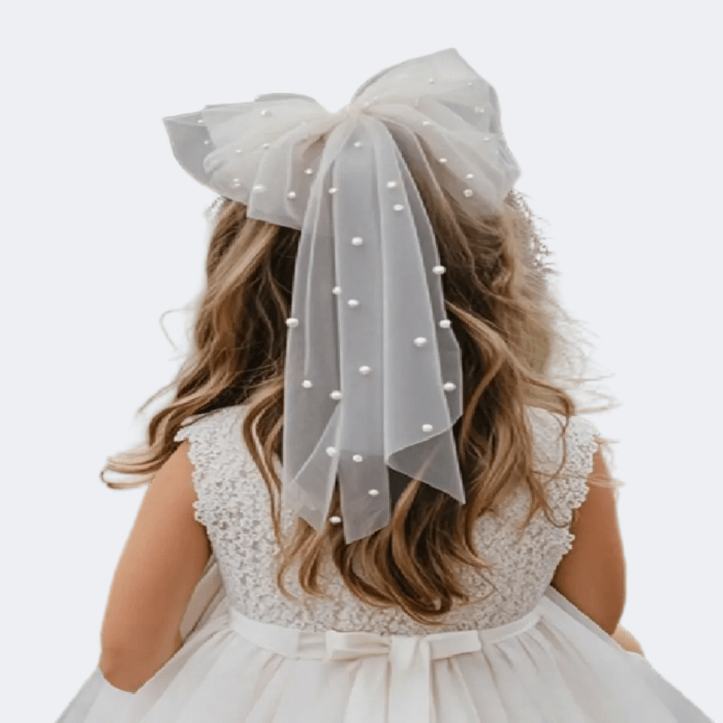 Child wearing a white lace dress with a large bow on a plain background