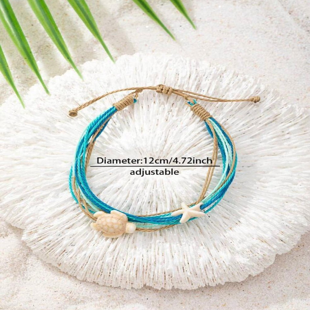 Blue and brown bracelet with turtle and starfish charms on a white shell