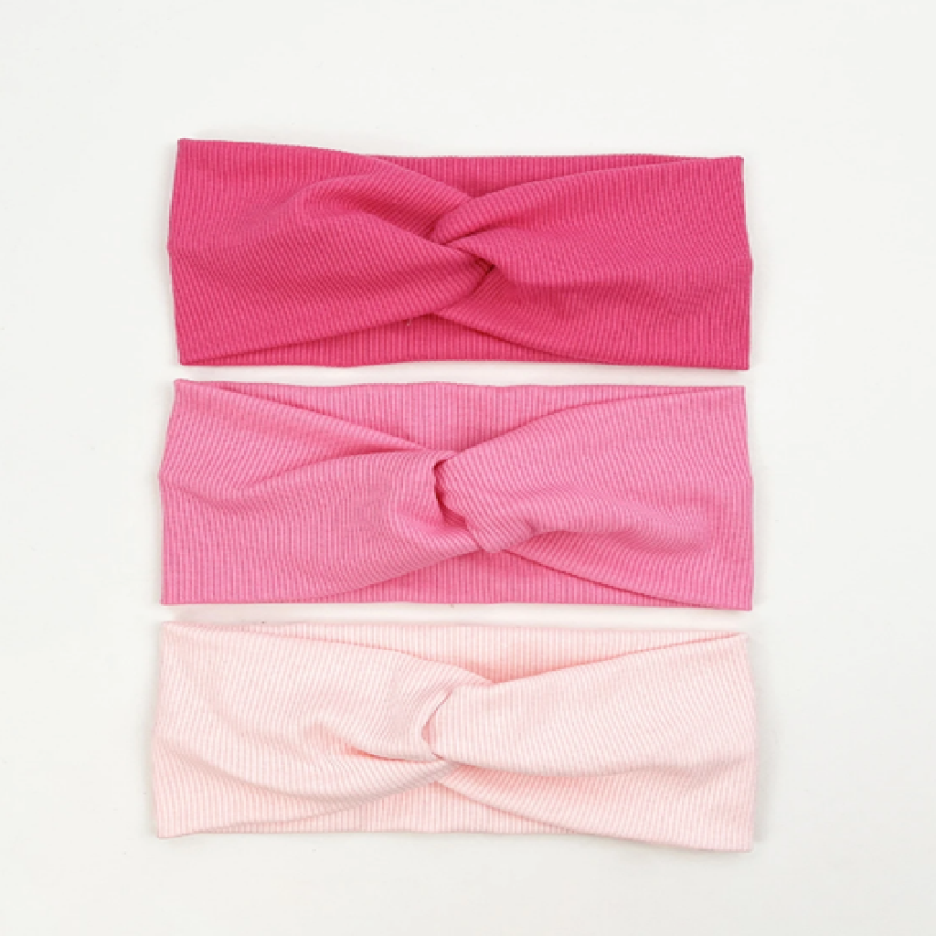 Three pink headbands with twisted designs on a white background
