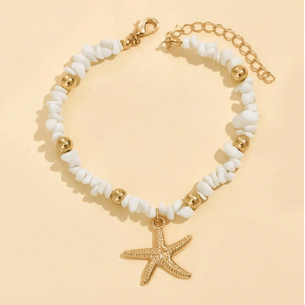Bracelet with white beads and gold starfish charm on a beige background