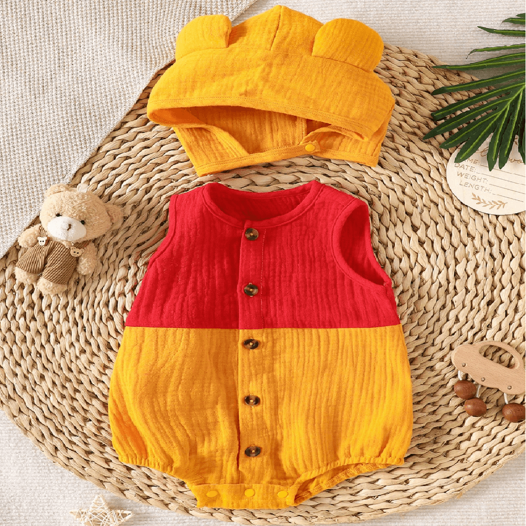 A baby romper and matching hat set laid flat on a woven mat. The romper is sleeveless with a red upper half and yellow lower half.