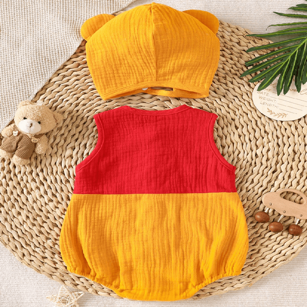 A baby romper and matching hat set laid flat on a woven mat. The romper is sleeveless with a red upper half and yellow lower half.