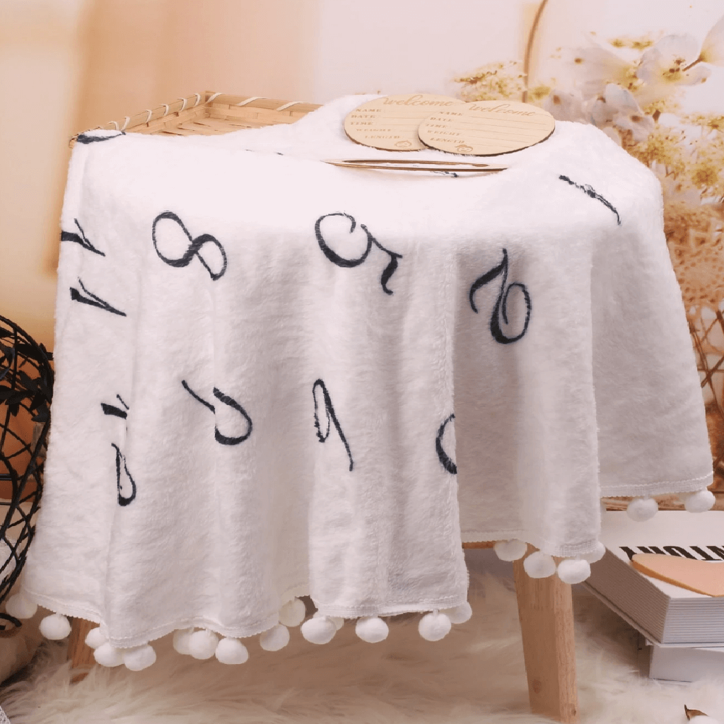 White tablecloth with black letter patterns and pom-poms on a wooden table.