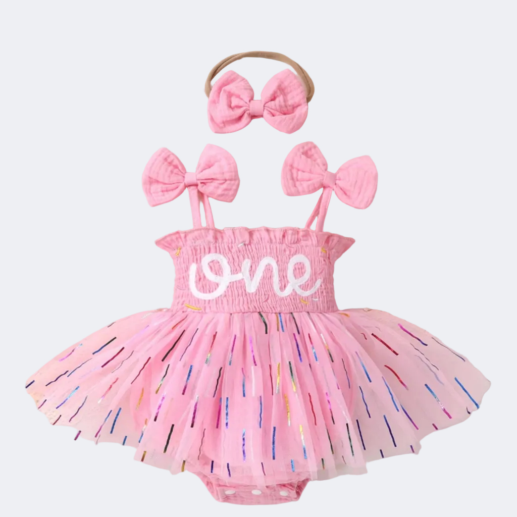 Pink baby romper with 'one' and bow accessories on a decorative background