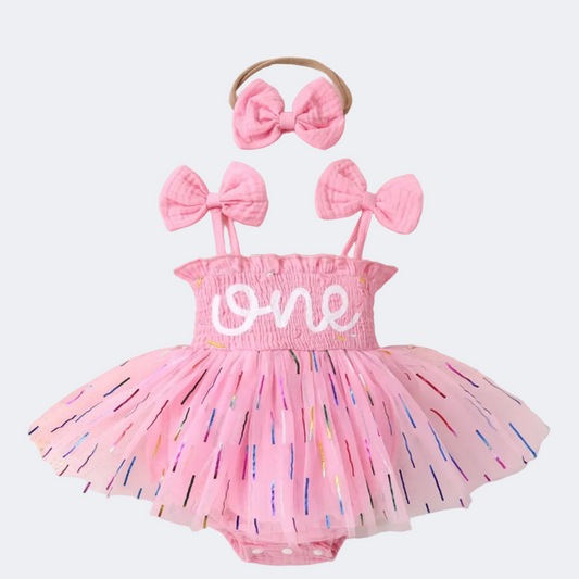 Pink baby romper with 'one' and bow accessories on a decorative background